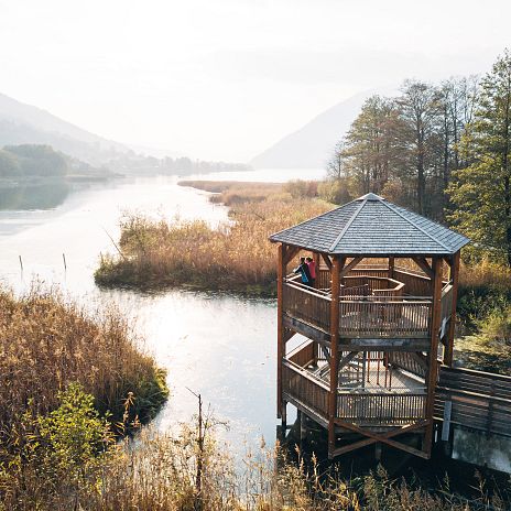 Eine Moorlandschaft. Berge im Hintergrund. Im Vordergrund eine hölzerne Aussichtsplattform um das Moor zu überblicken